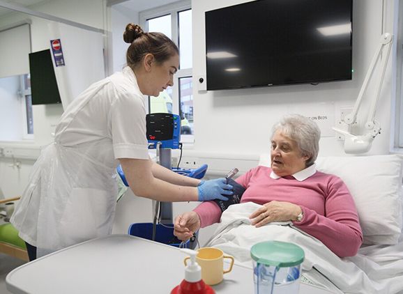 A nurse taking an elderly ladys blood pressure in a hospital bed