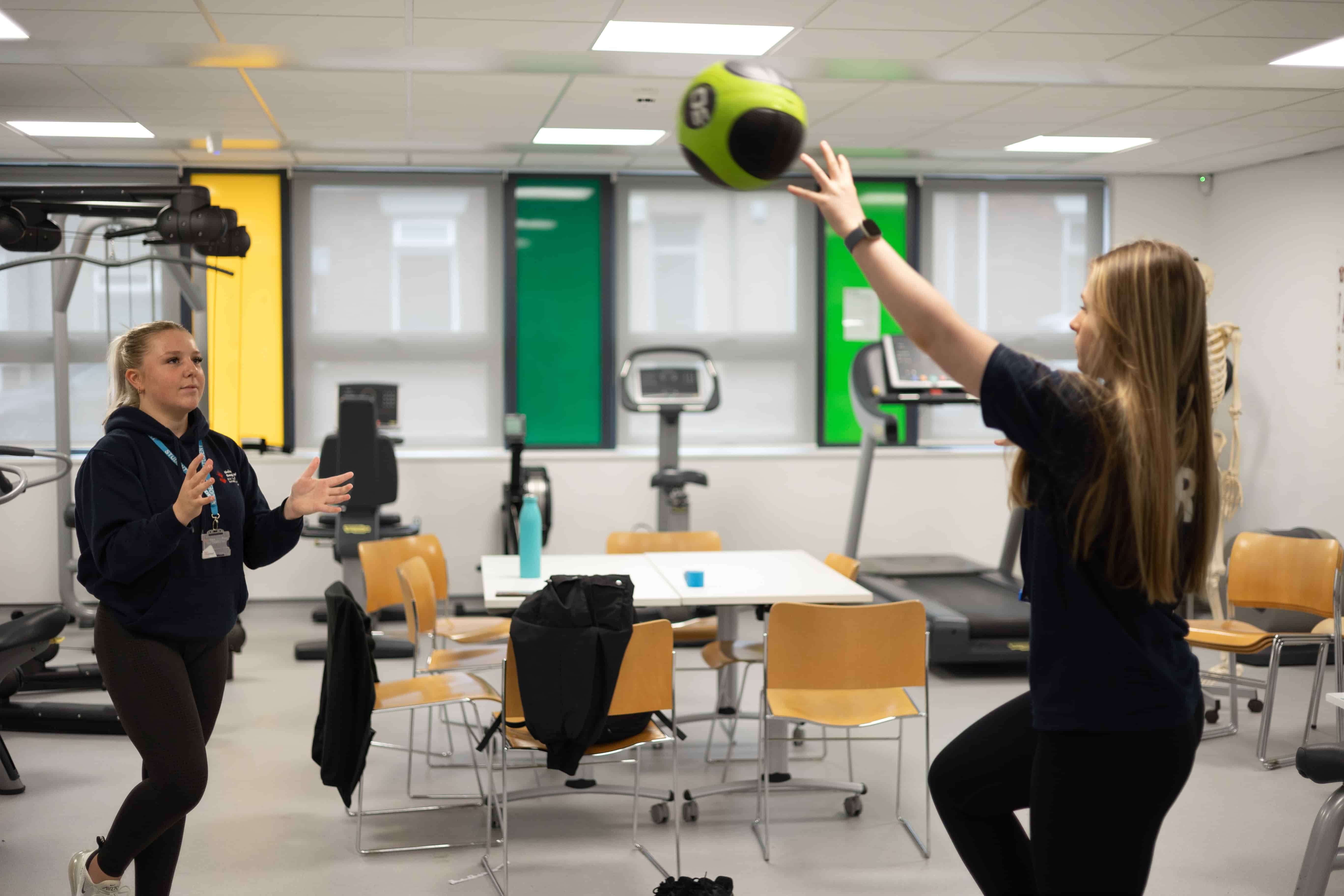 Two students throwing the medicine ball to one another in the gym