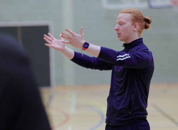 A student talking to people in a sports hall using his hands to demonstrate