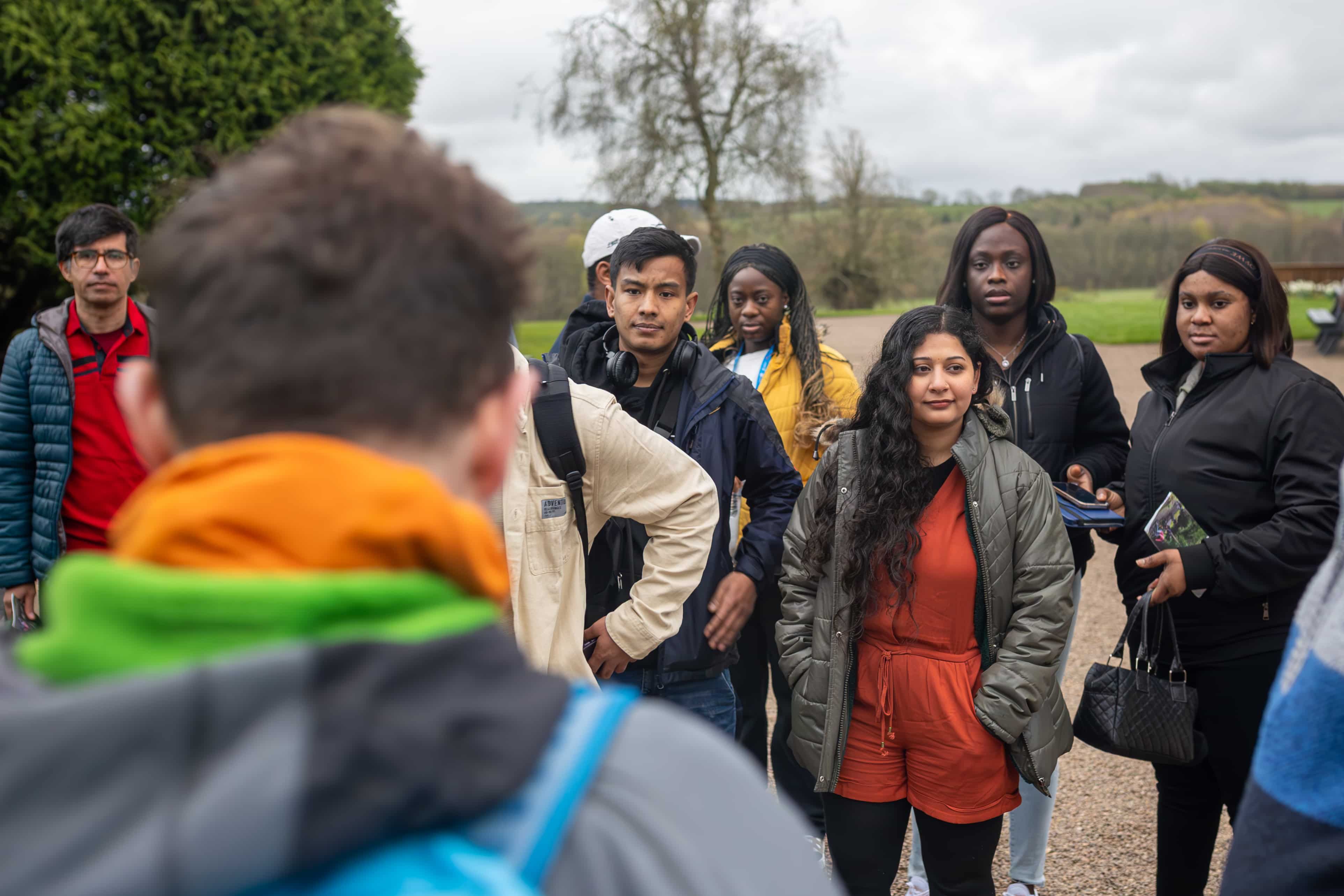 An over shoulder shot of students gathered on a field trip in the outdoors listening to the lecturer