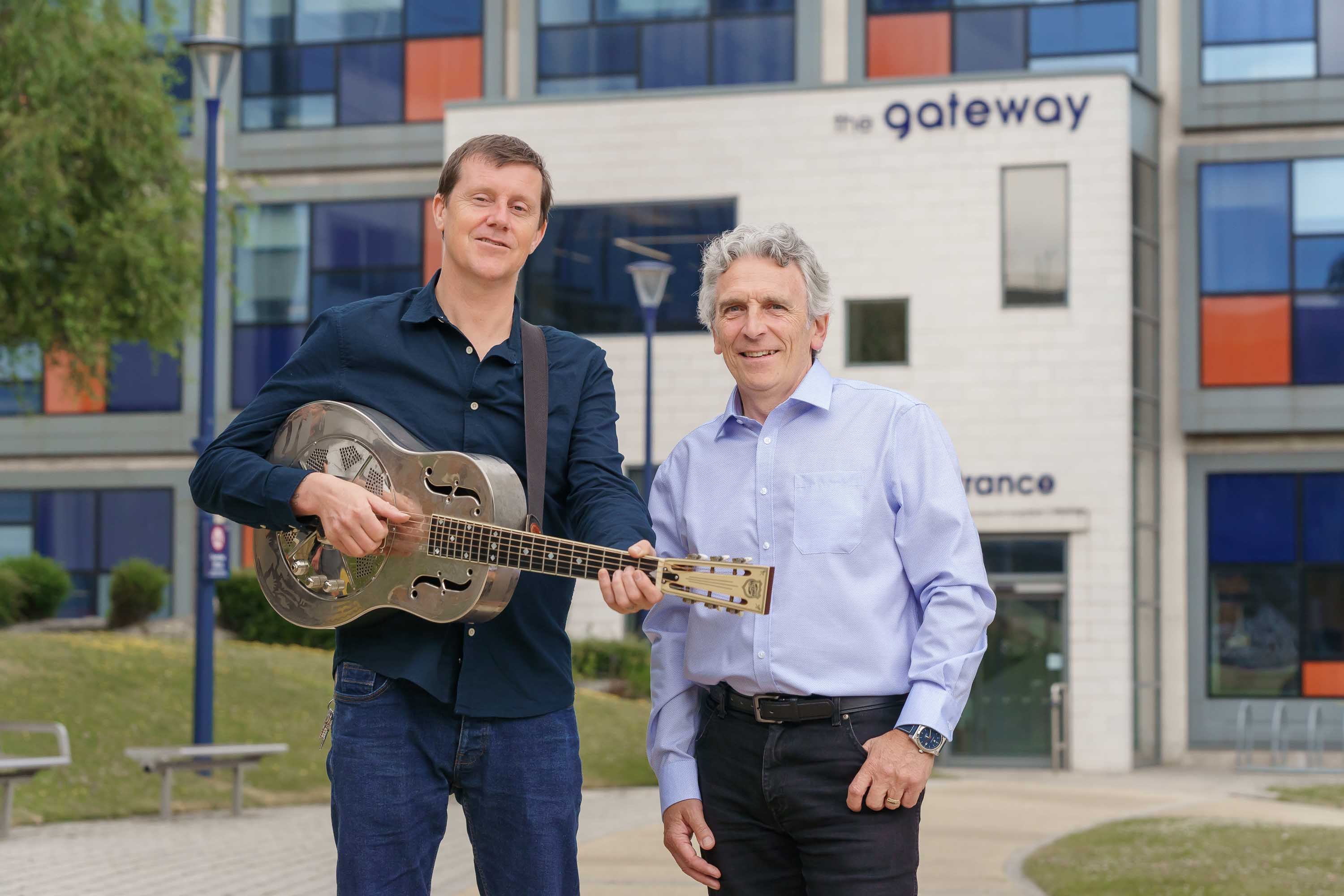 Richard O'Neill and George Hoyle stand outside of The Gateway building holding a guitar.