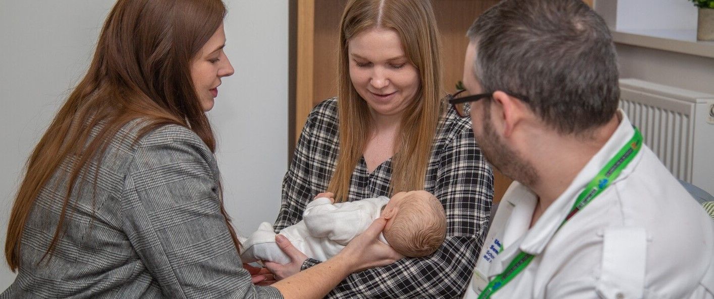 A parent holding a baby sat beside a nurse